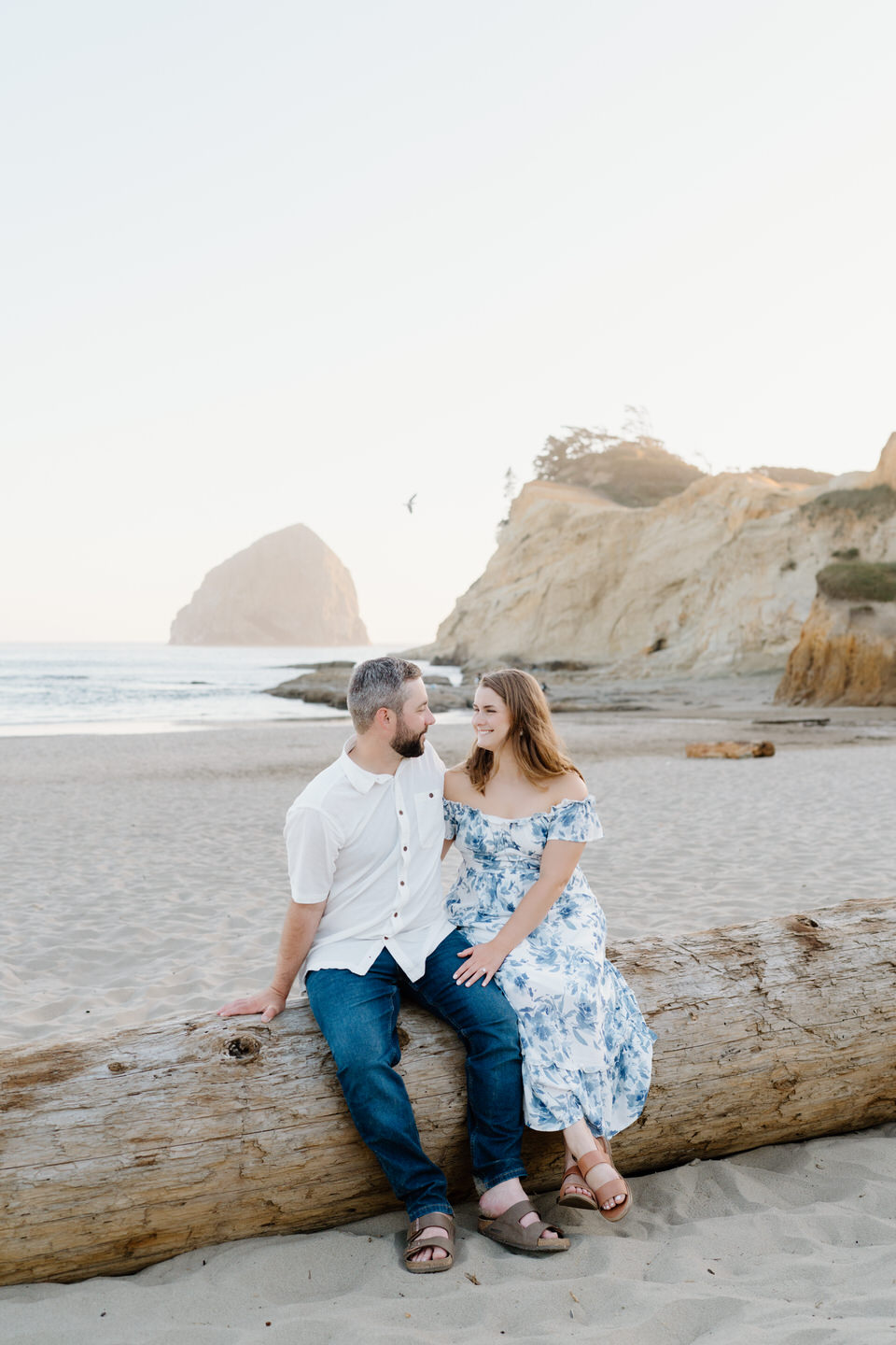 Couple sits on a driftwood log on the Oregon coast.