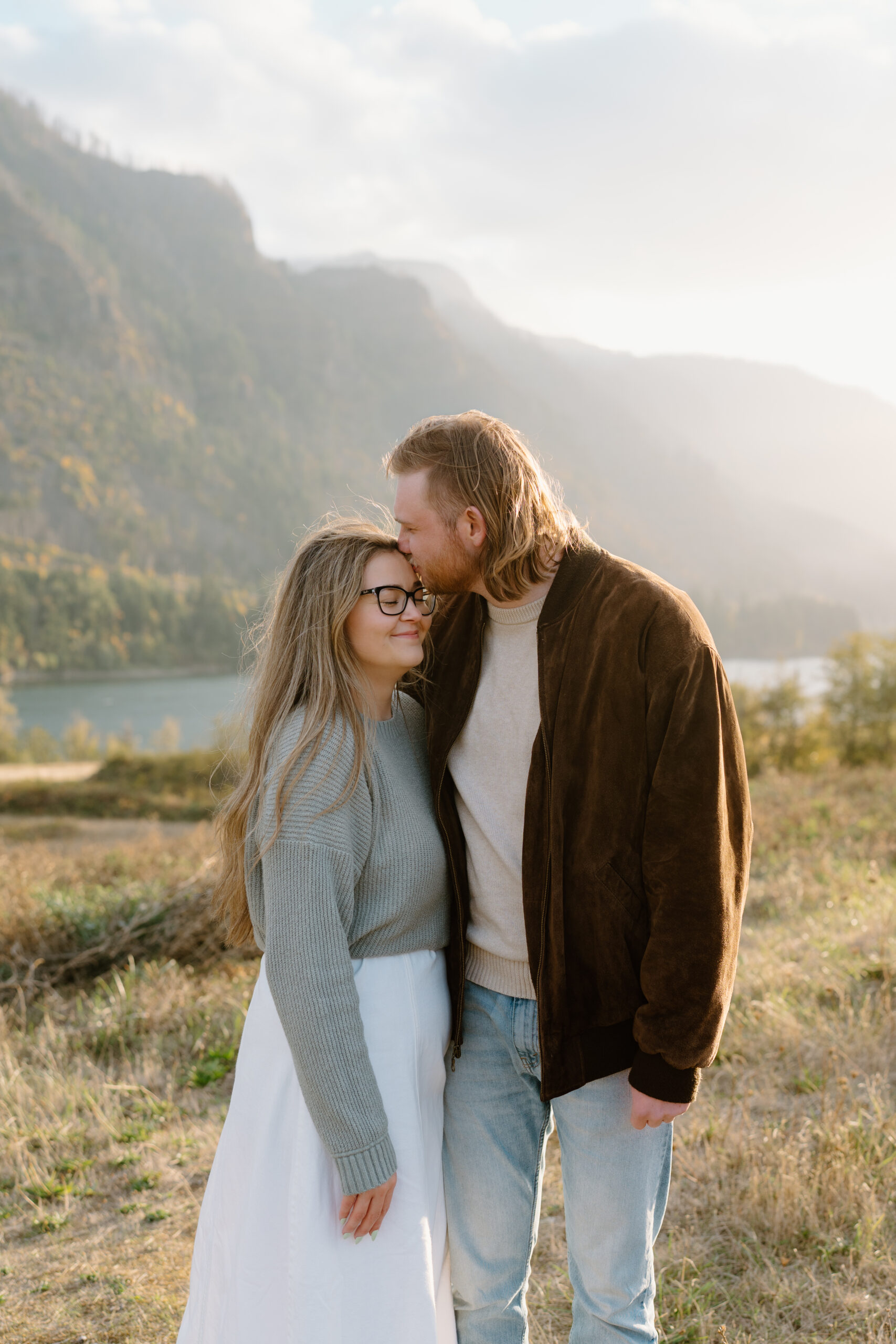 Man kisses woman on the forehead, draped in golden hour light.