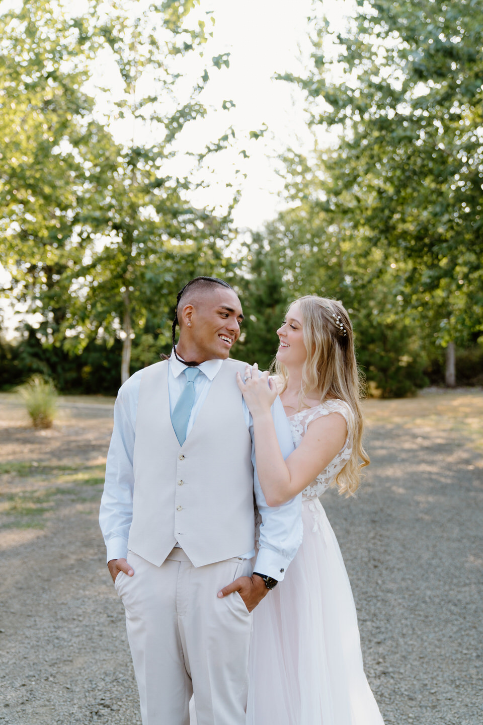 Bride looks lovingly at her groom while holding his shoulder with the golden hour sun in the background.