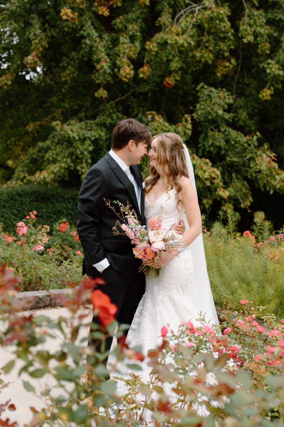 A tender forehead kiss shared by the couple, framed by soft petals and the bride’s pink bouquet.