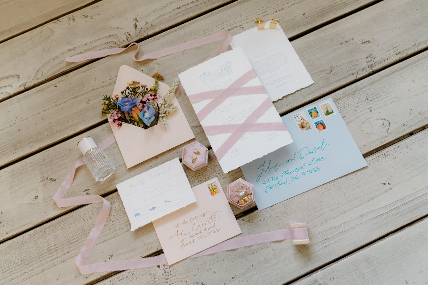 Wedding rings shine beside the invitation cards, surrounded by pastel florals and delicate paper textures.