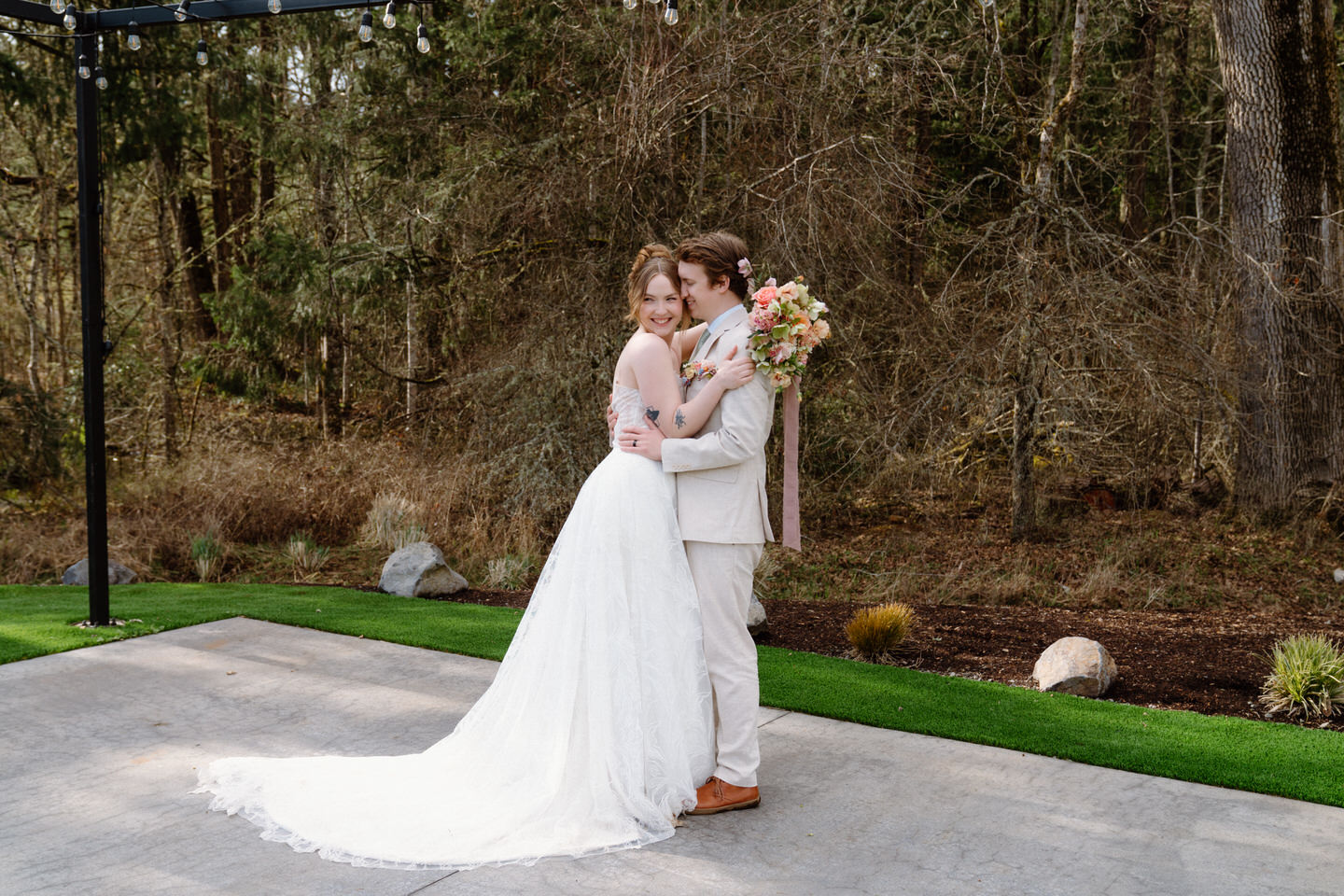 The couple hugs among the trees behind Sage & Social, ready for portraits in the quiet woods.