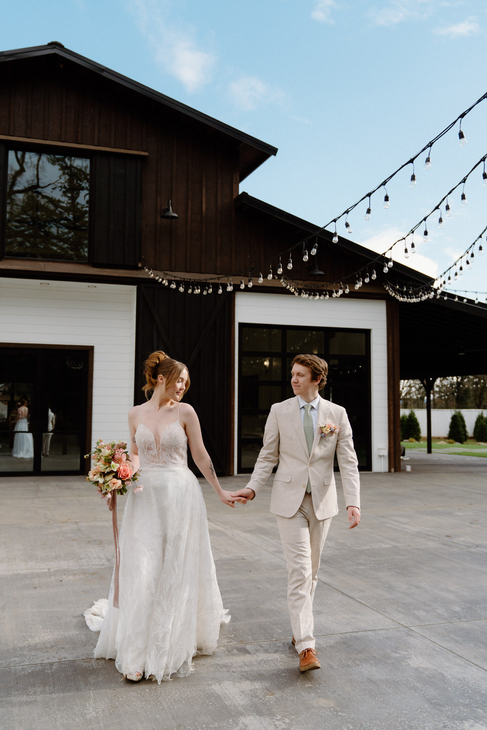 A couple shares a joyful moment in front of Sage & Social’s black barn doors, the dress catching wind.