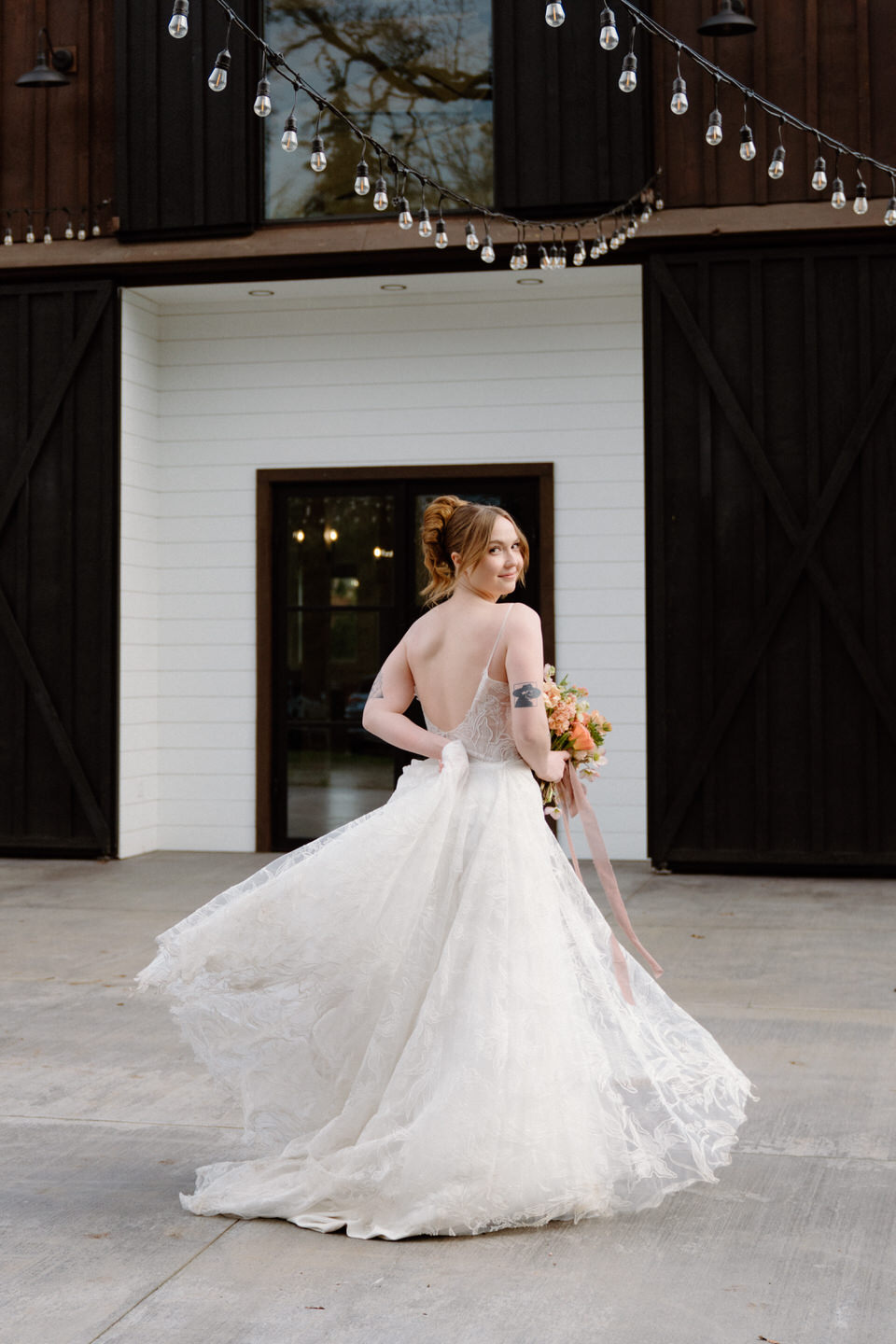 A bride twirls in her Madi Lane gown as her partner spins her outside the dark barn at Sage & Social.