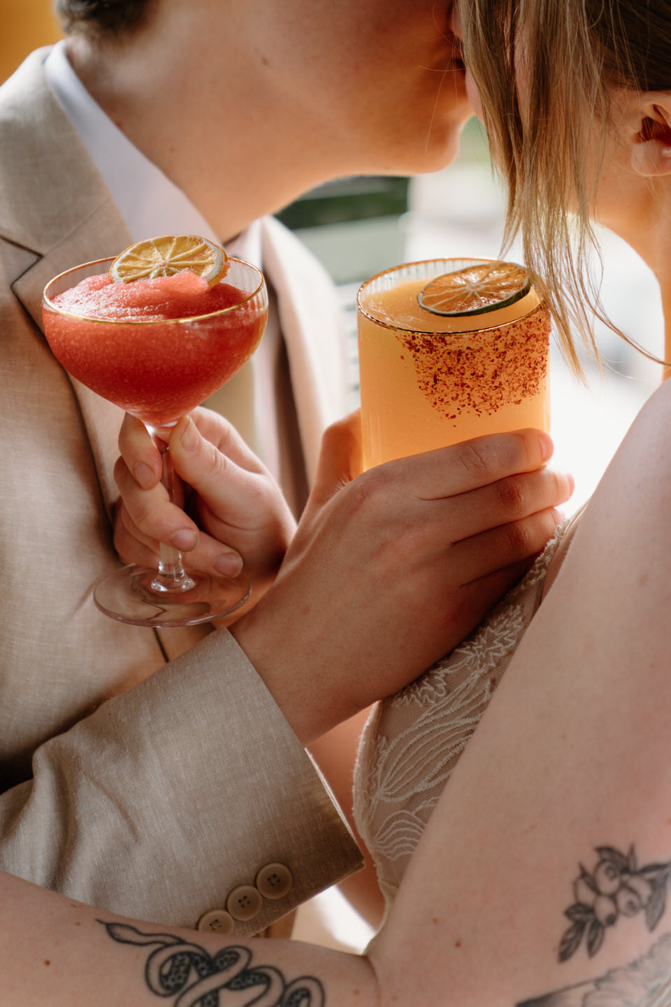 A close-up of the couple’s hands holding a margarita and daiquiri, the colorful frozen drinks catching the light.