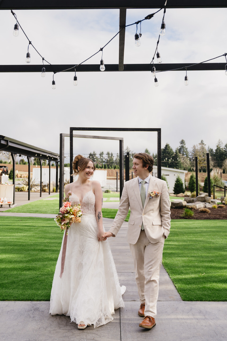 Gabby walks hand-in-hand with Hunter through square archways at Sage & Social, surrounded by woodlands.