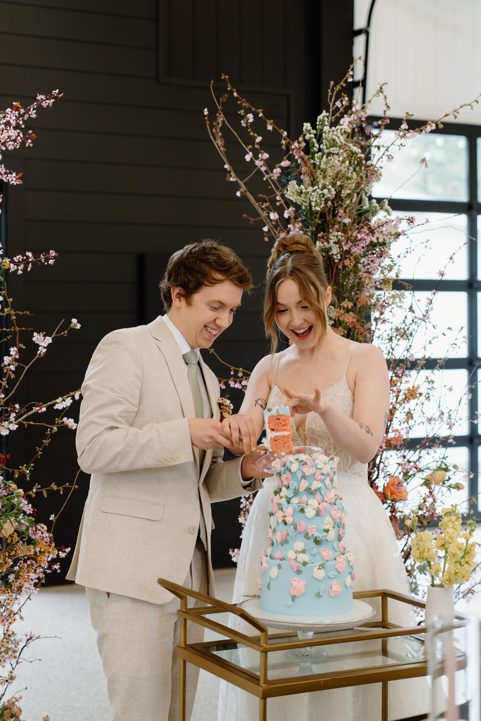 A joyful cake cutting moment inside Sage & Social’s reception barn, framed by soft lighting and florals.