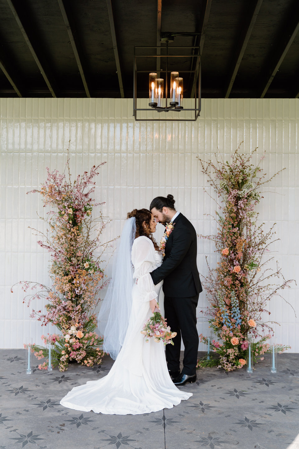 A couple stands forehead to forehead at Sage & Social, wrapped in soft spring light and romantic florals.