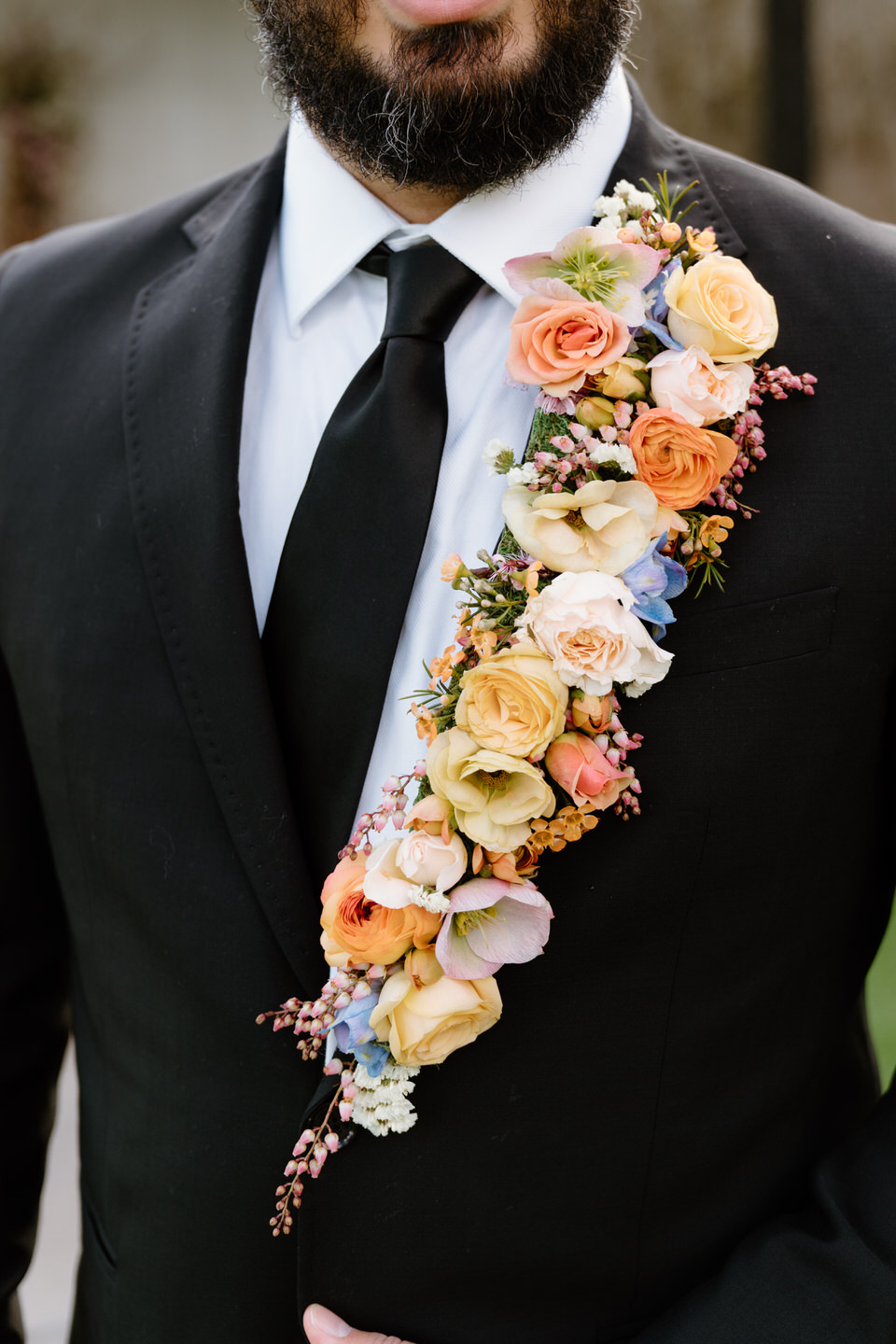 A cascading boutonniere makes a bold statement against a black suit and neutral modern backdrop.