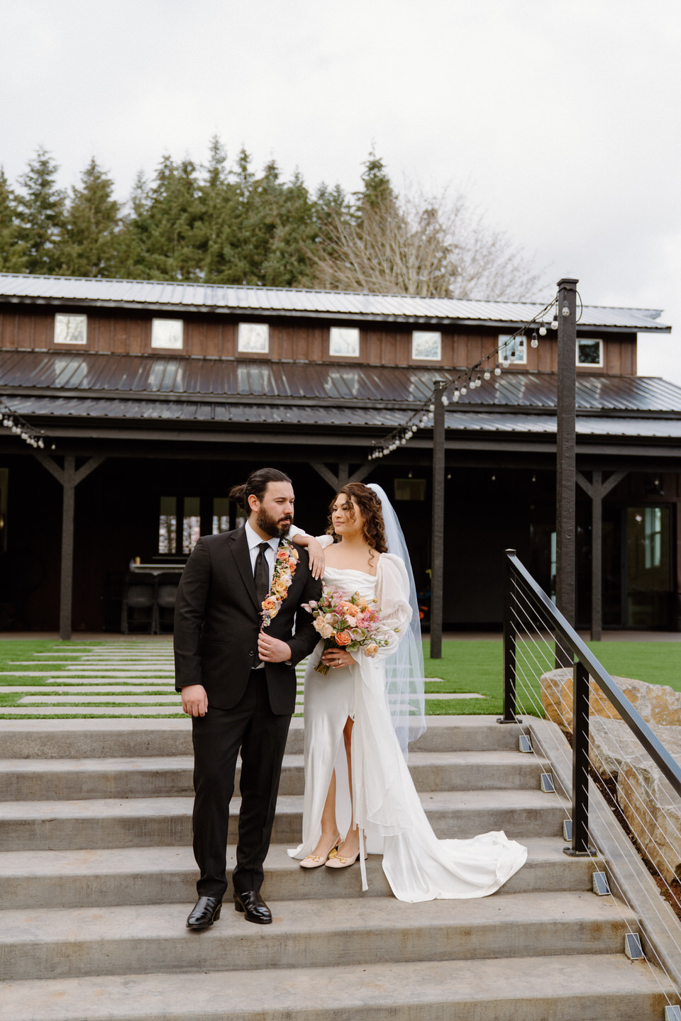 The groom stands beside his bride, the black suit and cascading boutonniere contrasting beautifully against her soft gown.