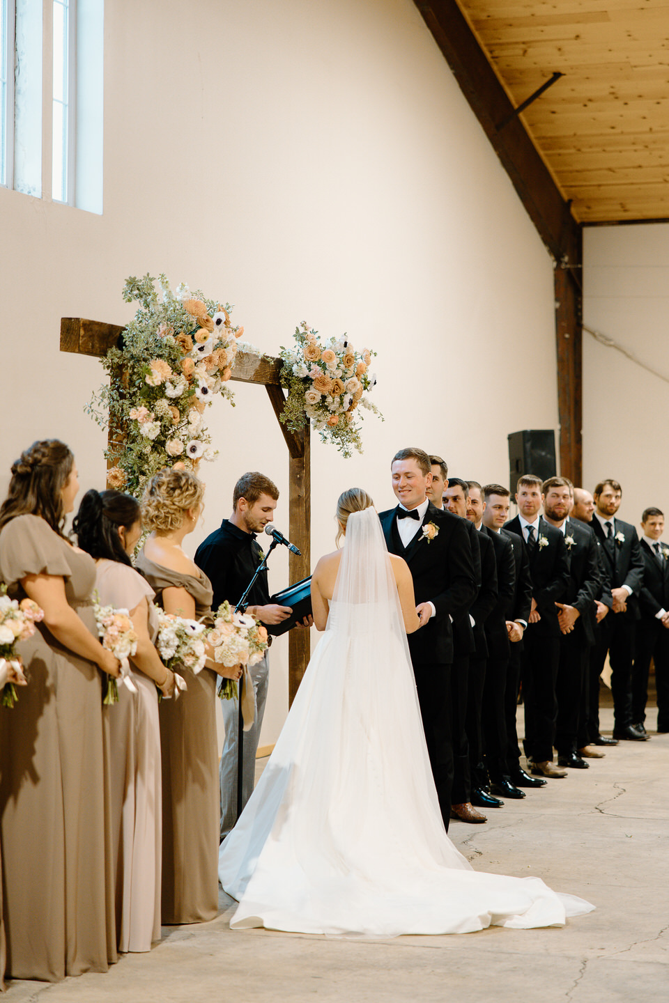 Groom smiles eagerly at his bride during their indoor wedding ceremony.