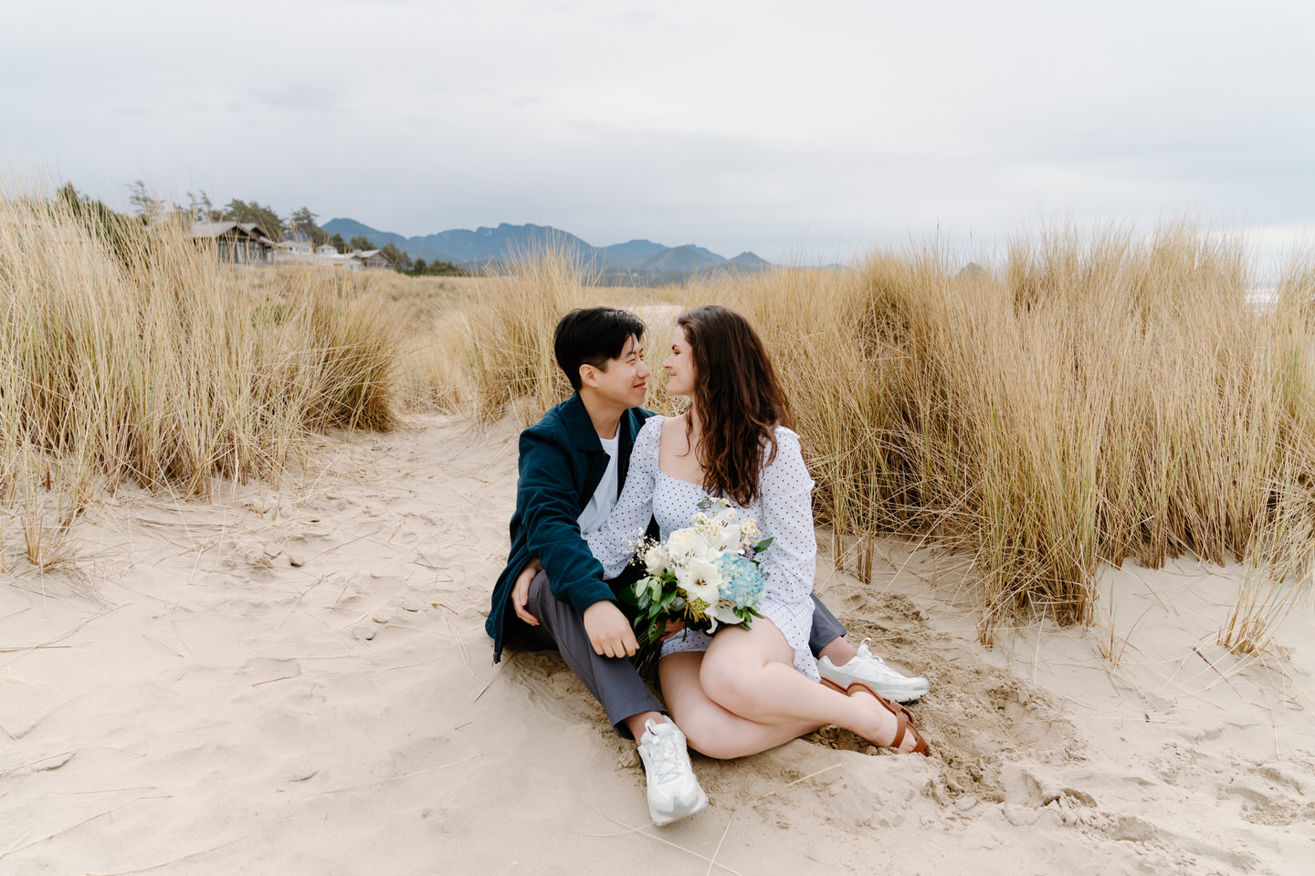 Couple snuggling together on the sand during Cannon Beach engagement shoot.