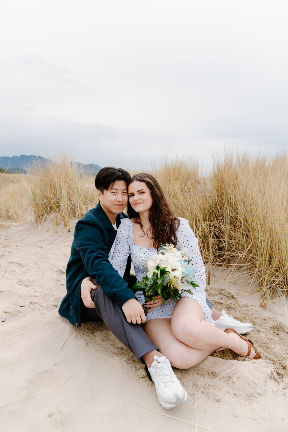 Couple sitting on the sand with moody skies and distant rock formations.