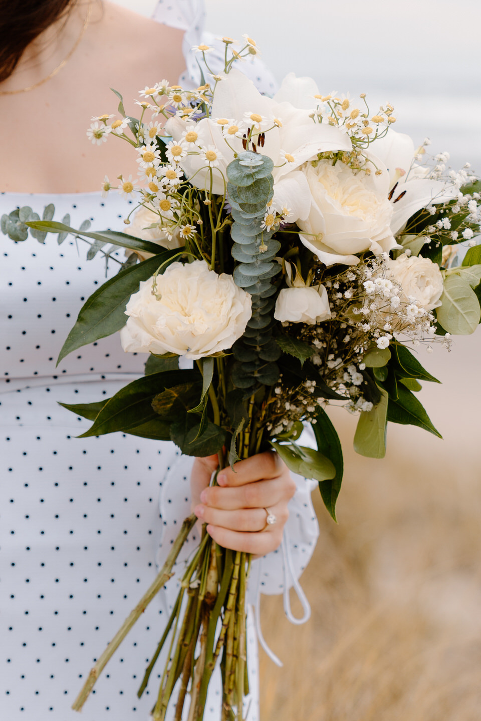 White bouquet of roses and eucalyptus held during coastal engagement session.