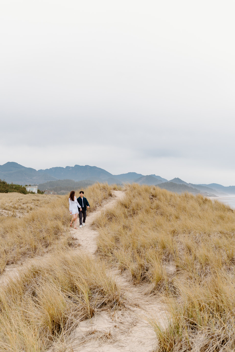 Couple holding hands with ocean and tall grass in the background on the Oregon Coast