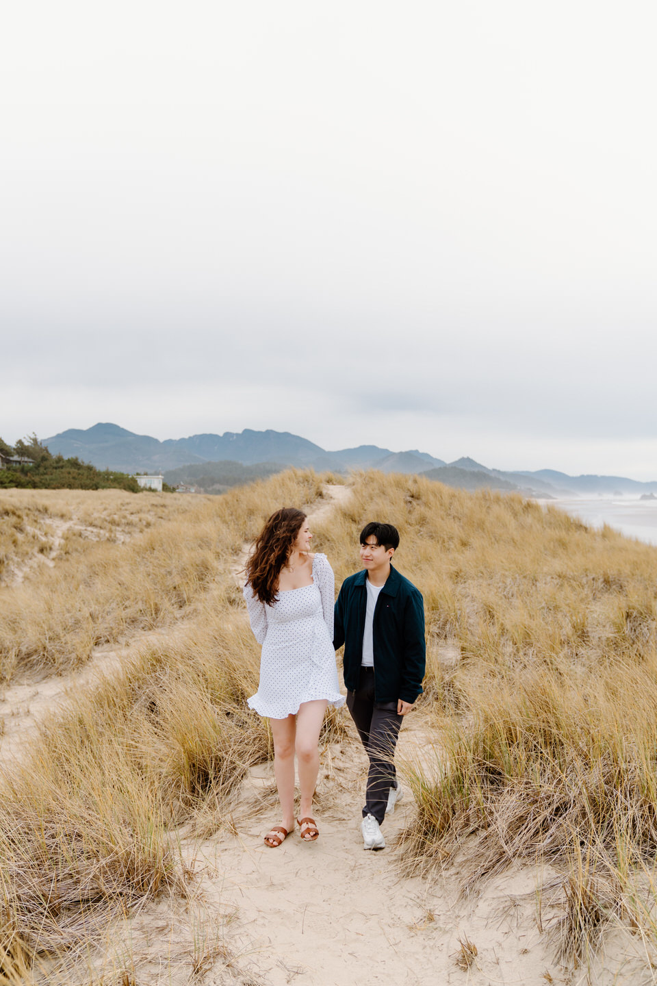 Couple walks through grassy hills during Oregon coast engagement photo session.