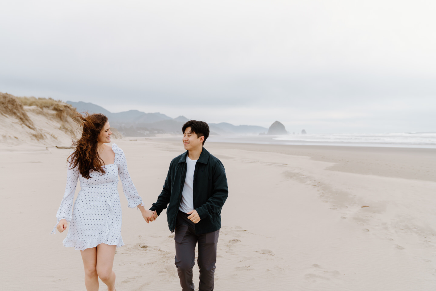 Couple walking hand-in-hand along a sandy trail near the ocean.