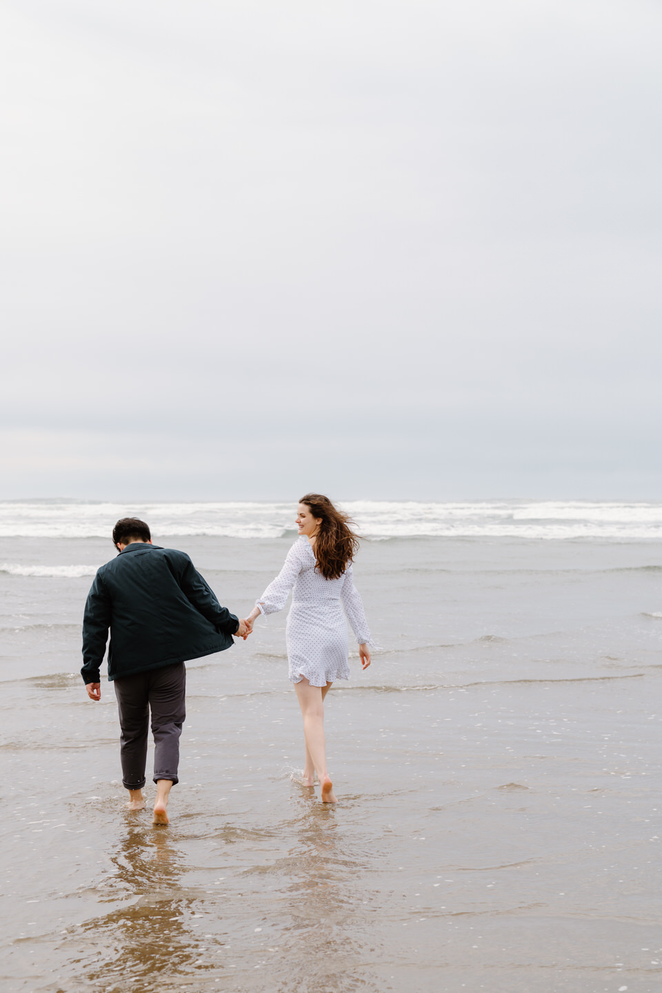 Laughing couple walking hand-in-hand along the Oregon Coast shoreline.