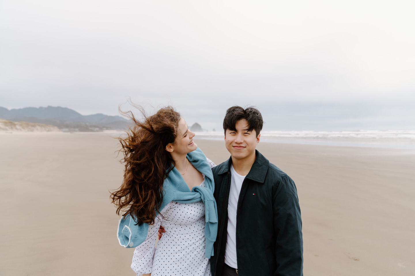 Playful shot of couple holding hands and laughing on the beach.
