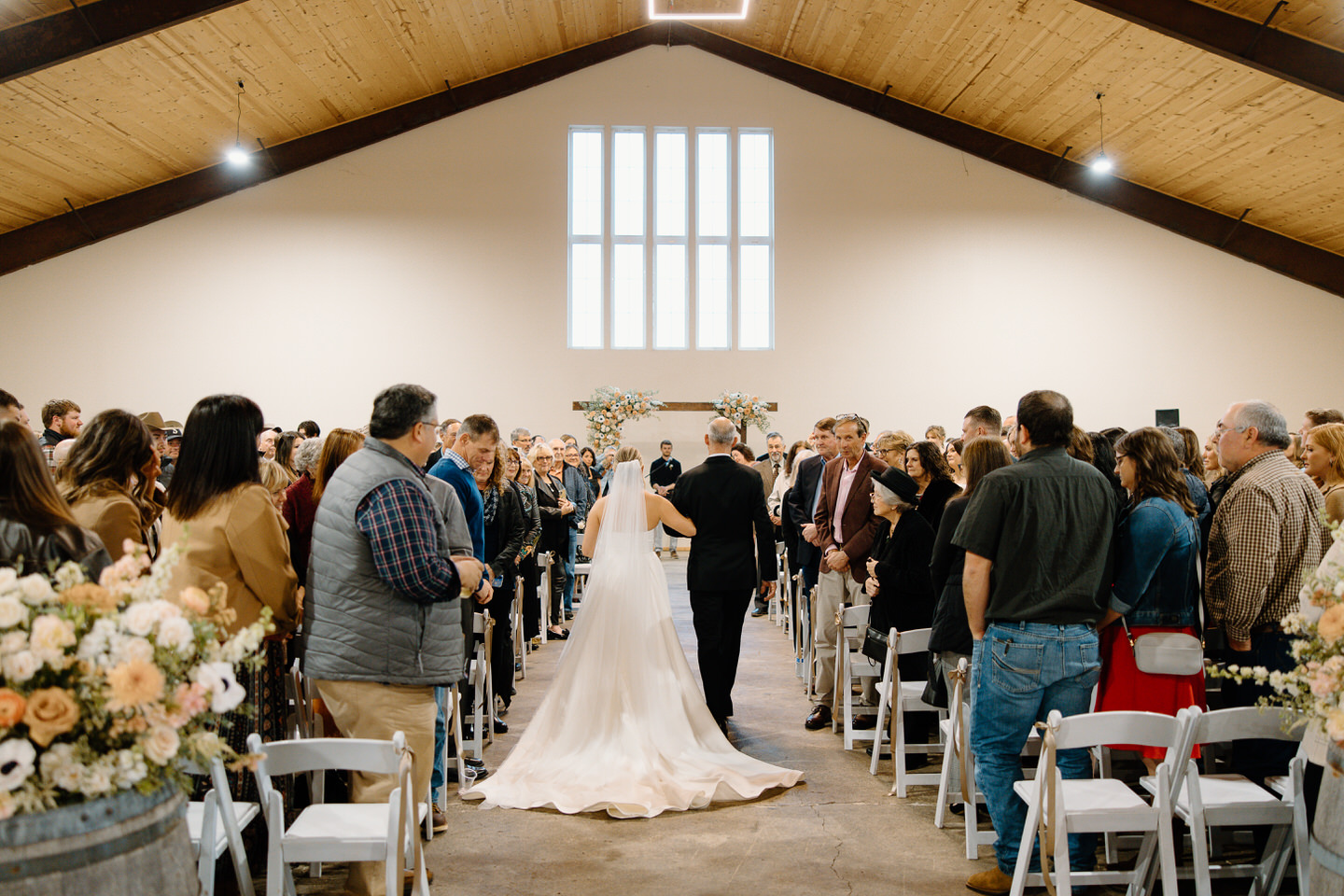 Guests stand inside The Barn at Countryside as the bride walks down the aisle.