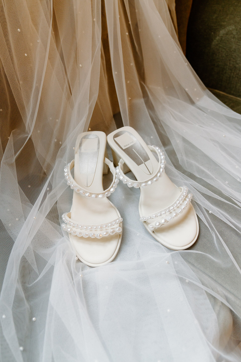 Bride's white heels, accented with pearls, laid on top of her veil.