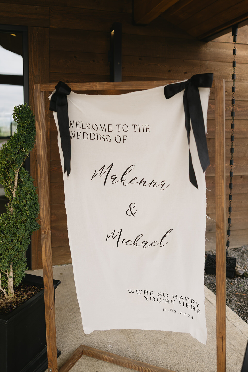 Linen wedding welcome sign with wood frame and black bows at the top.