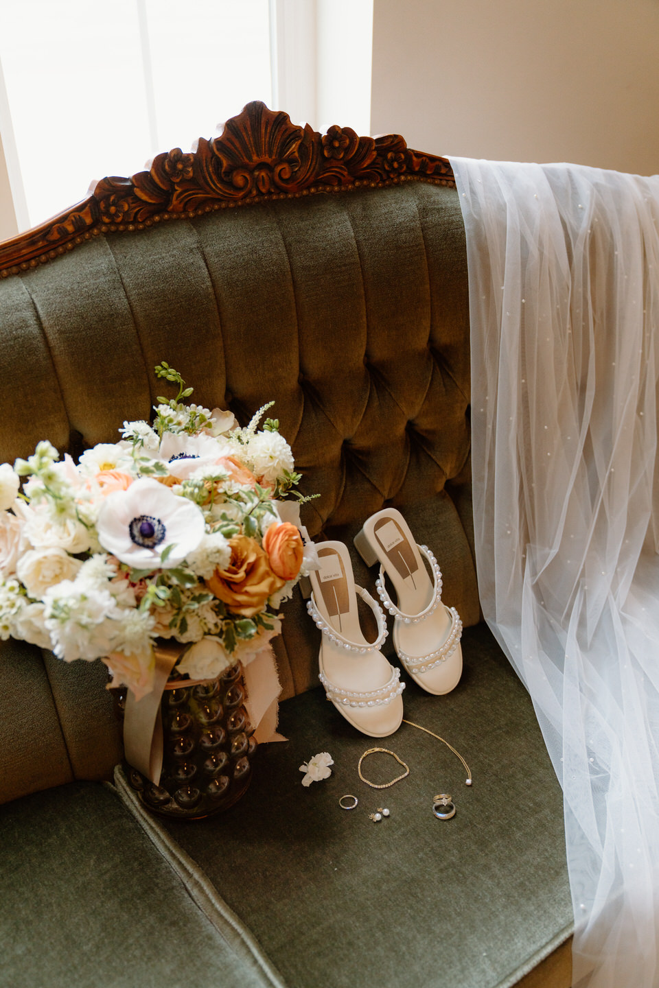 The bride's details thoughtfully laid out on a vintage green velvet couch.
