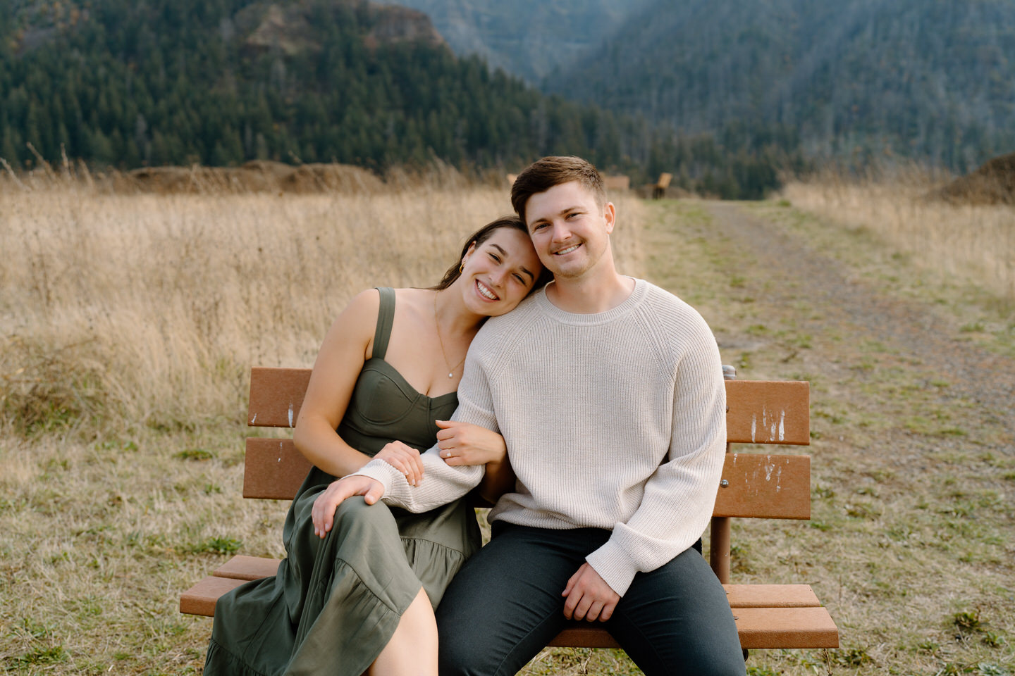 Woman in sage green dress and man in brown jacket smiling at camera — fall engagement outfit inspiration.