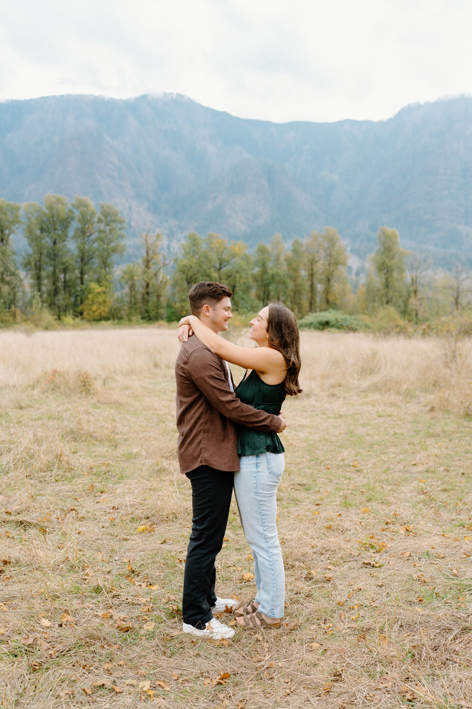Wide shot of couple standing in open field, mountains faint in the background — soft fall engagement in the Gorge.
