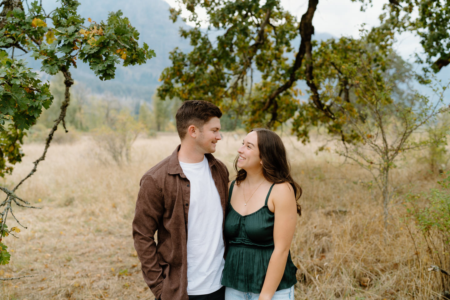 Couple laughing together with Columbia River Gorge cliffs in the background — candid fall engagement session.
