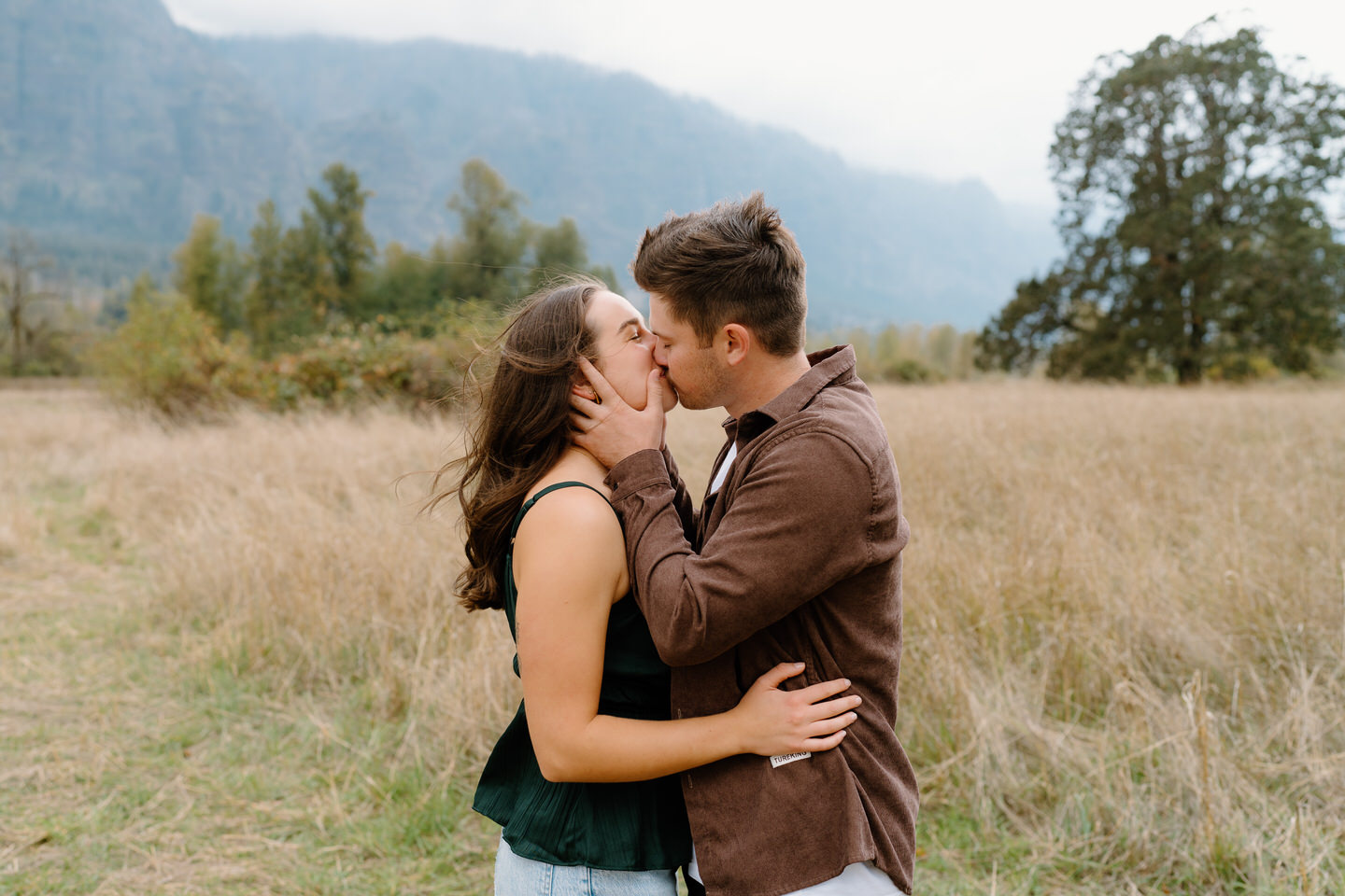Couple leaning in for a kiss surrounded by autumn grass and trees — cozy Columbia Gorge engagement session.