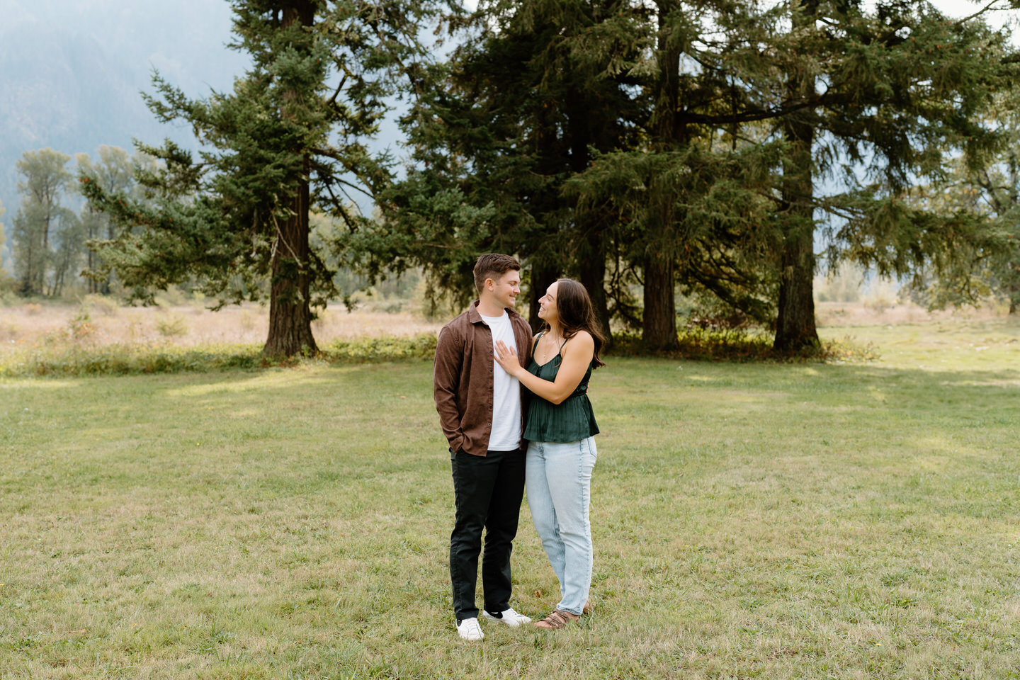 Woman leaning into her fiancé with a soft smile, showcasing fall engagement outfits in forest tones.