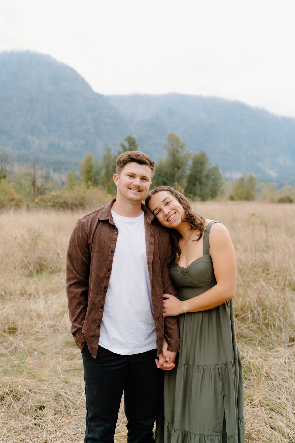 Woman resting her head on fiancé’s shoulder, both looking joyful — fall engagement photo in natural tones.