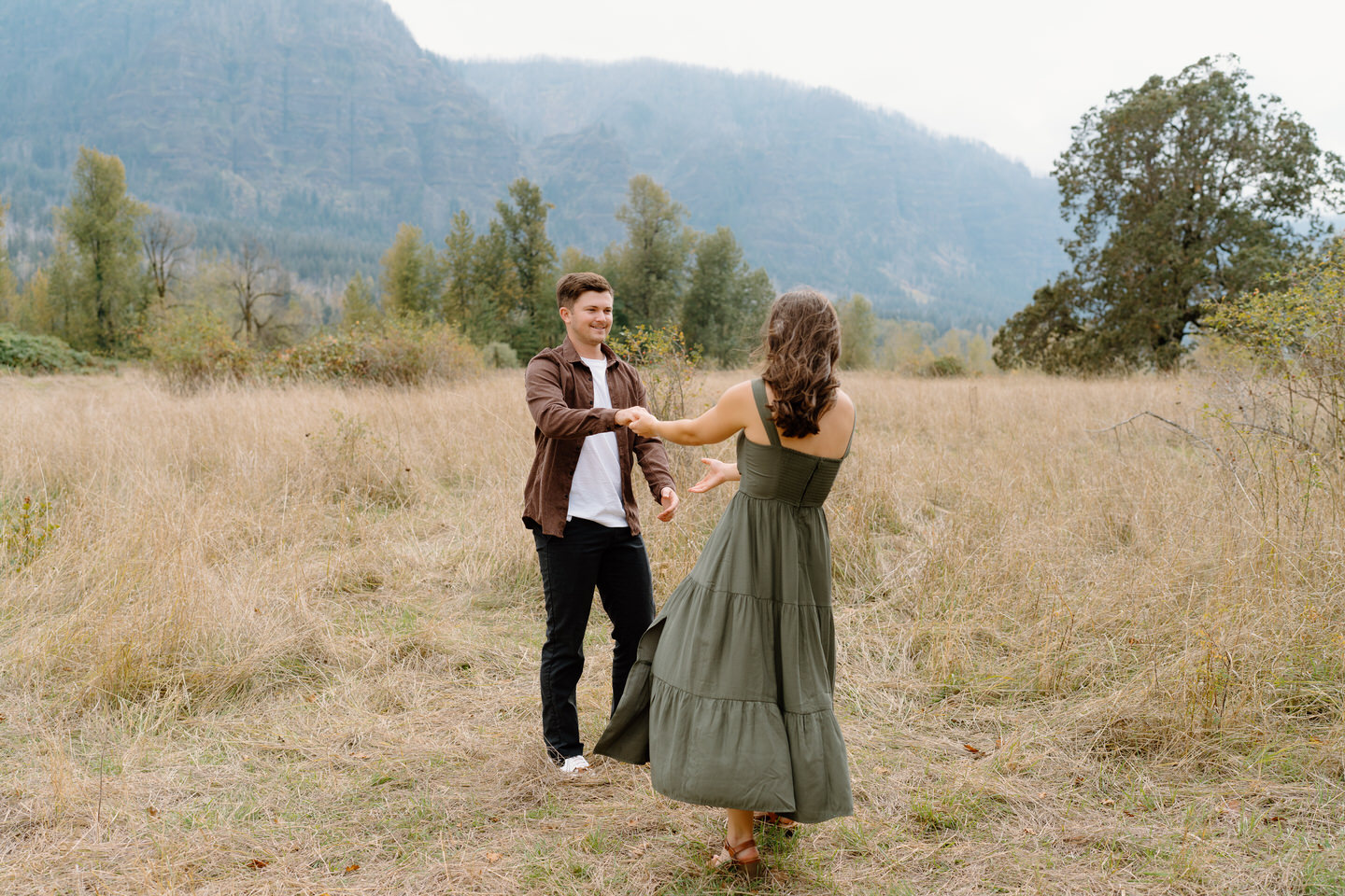 Couple dancing in a grassy field with overcast skies and soft autumn light — natural fall engagement photos in the Columbia Gorge.