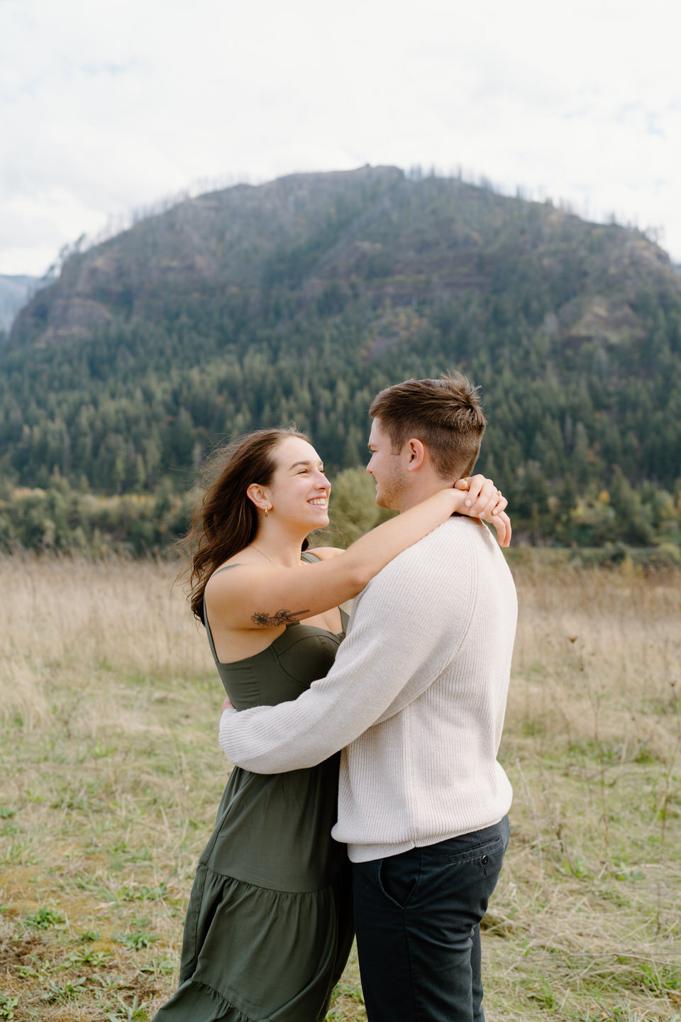 Couple embracing in an open field with mountain backdrop — fall engagement photos in the Columbia Gorge.