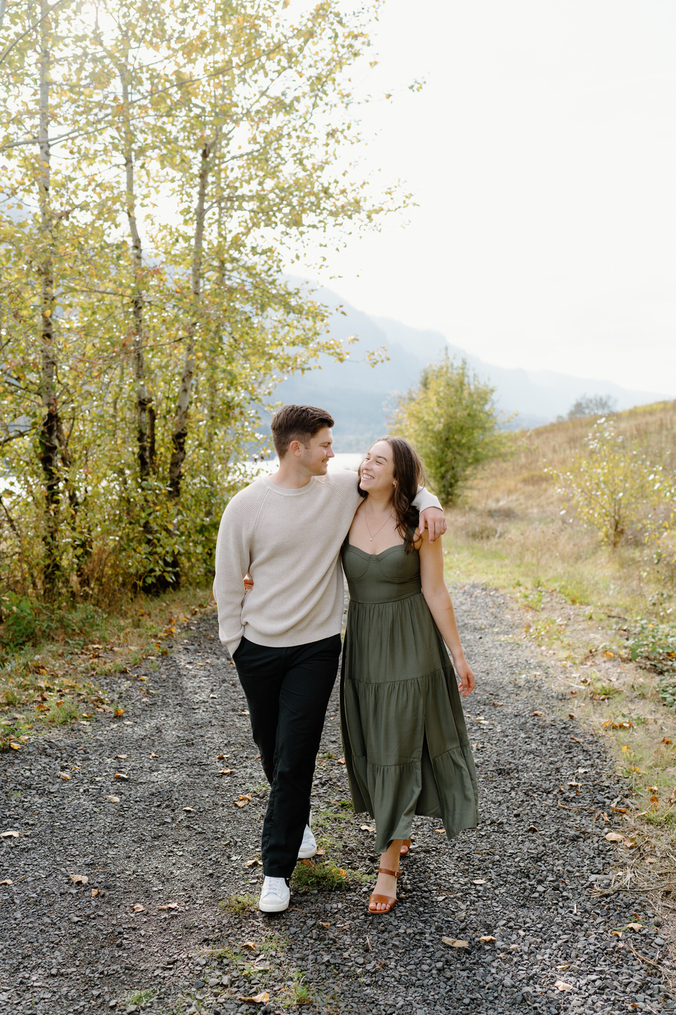 Woman in a green dress and man in a beige sweater smiling at each other — fall engagement outfits in the Columbia Gorge.