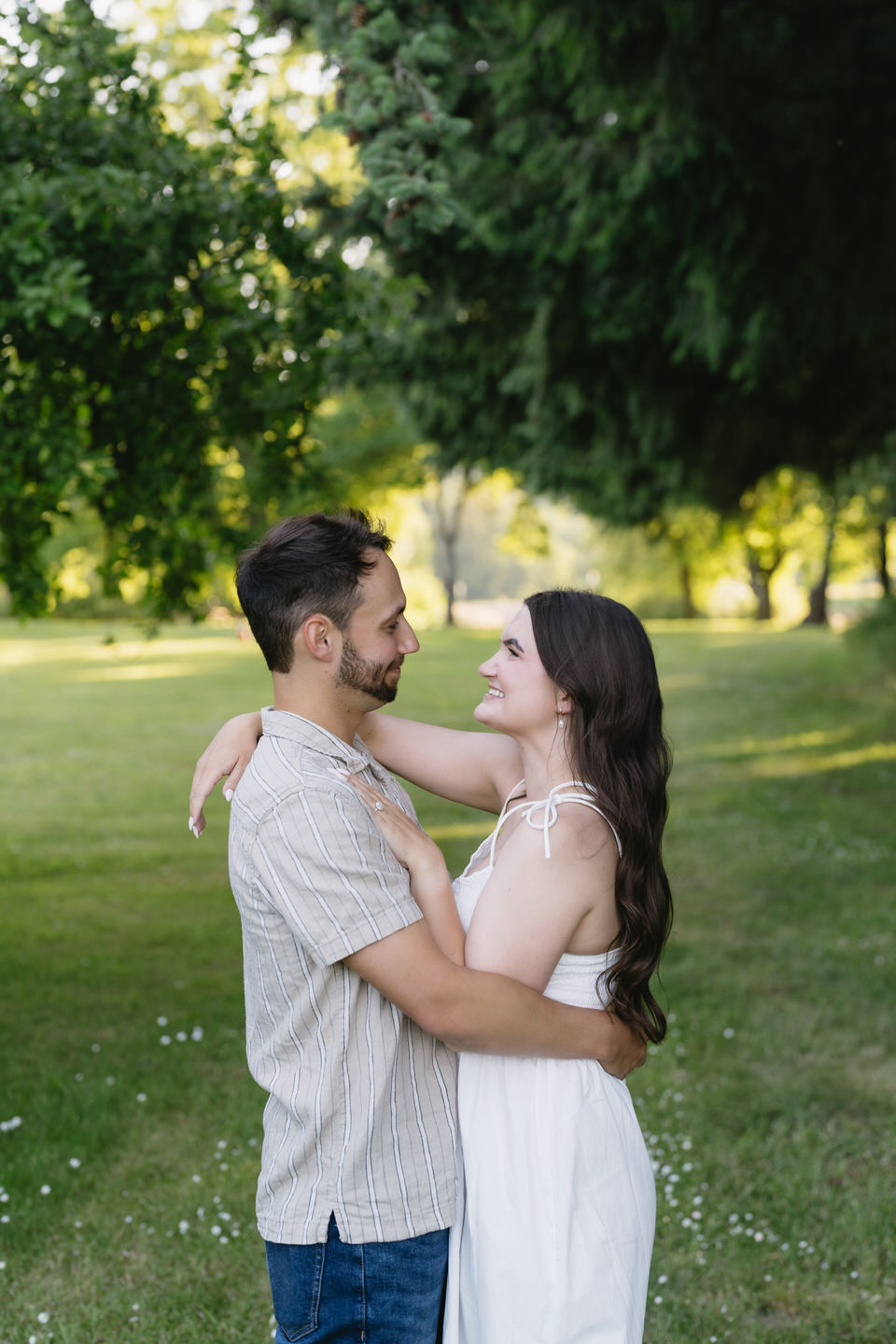 Woman in white dress and man in beige shirt surrounded by grass and trees.