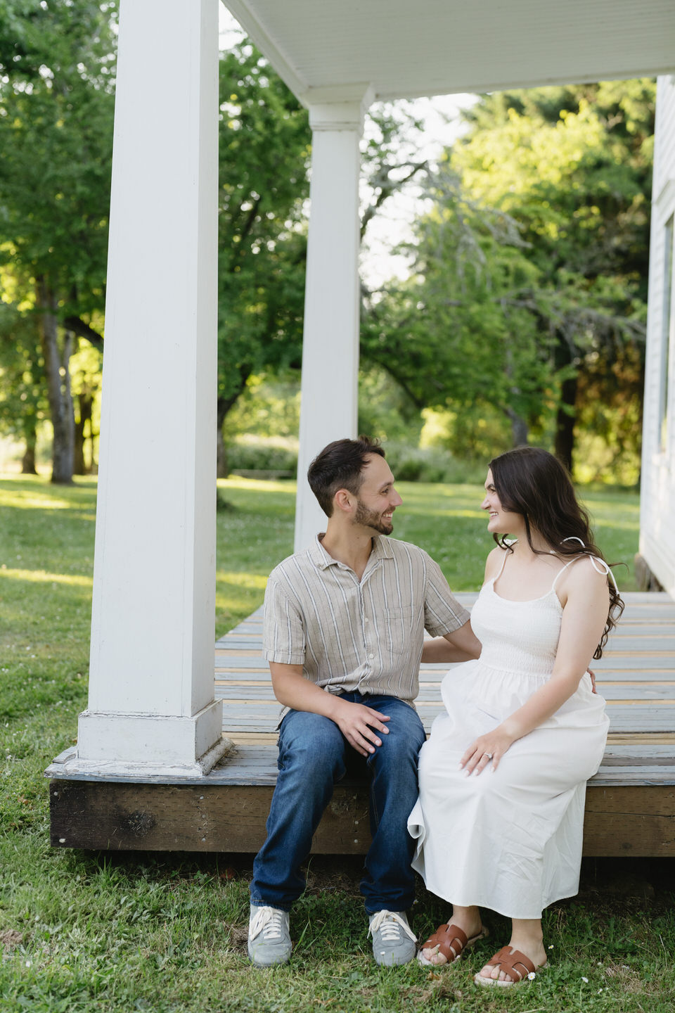 Couple sit together on the porch of a house, giving southern homestead vibes for their couples photos.