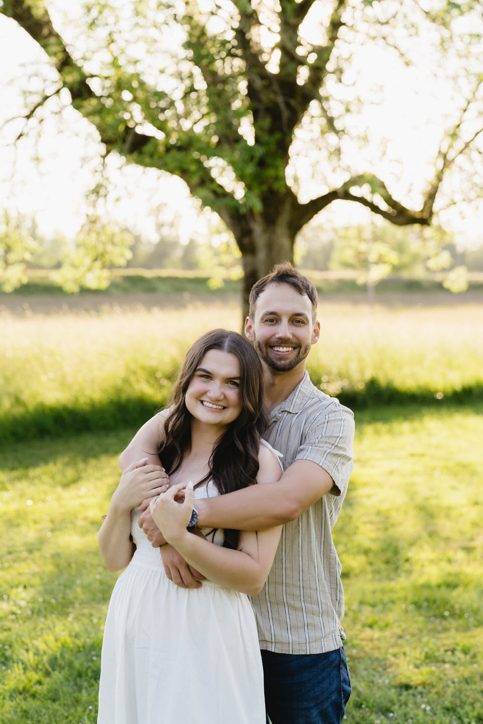 Man wraps his arm around his fianceé from behind.