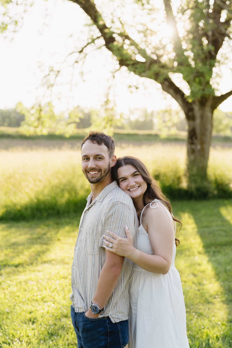 Woman leans her head on her fiancé's shoulder, both smiling at the camera.