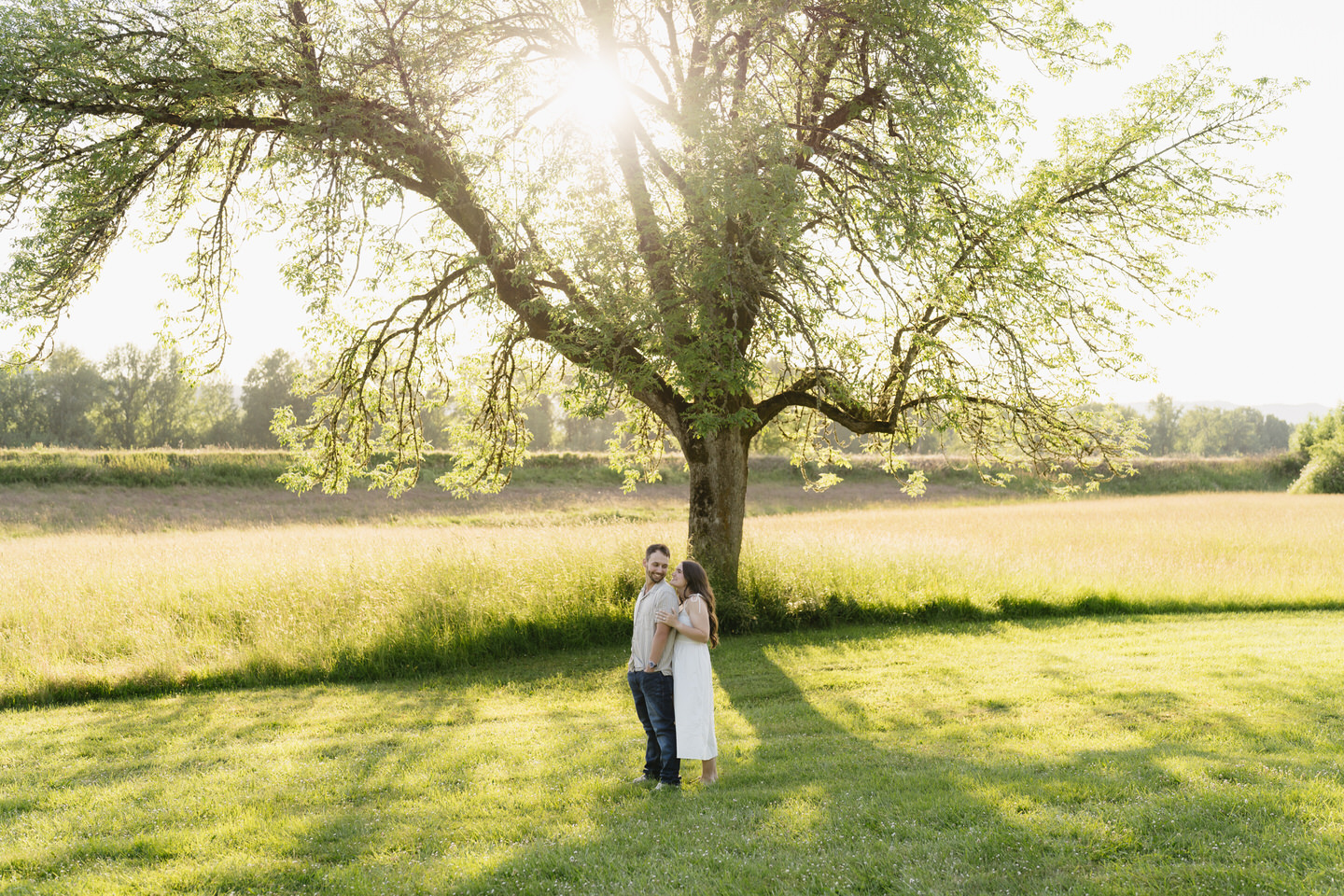 Couple stands together, appearing small under the large tree at Sauvie Island.
