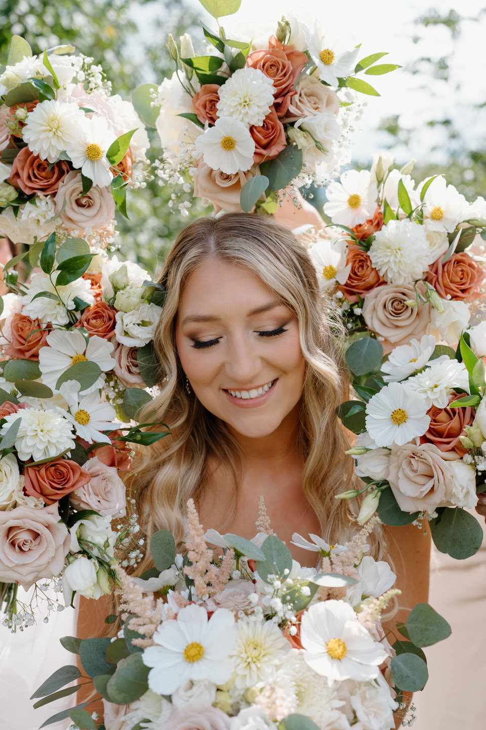 Bride beaming down at her bouquet, surrounded by the flowers of her bridesmaids.