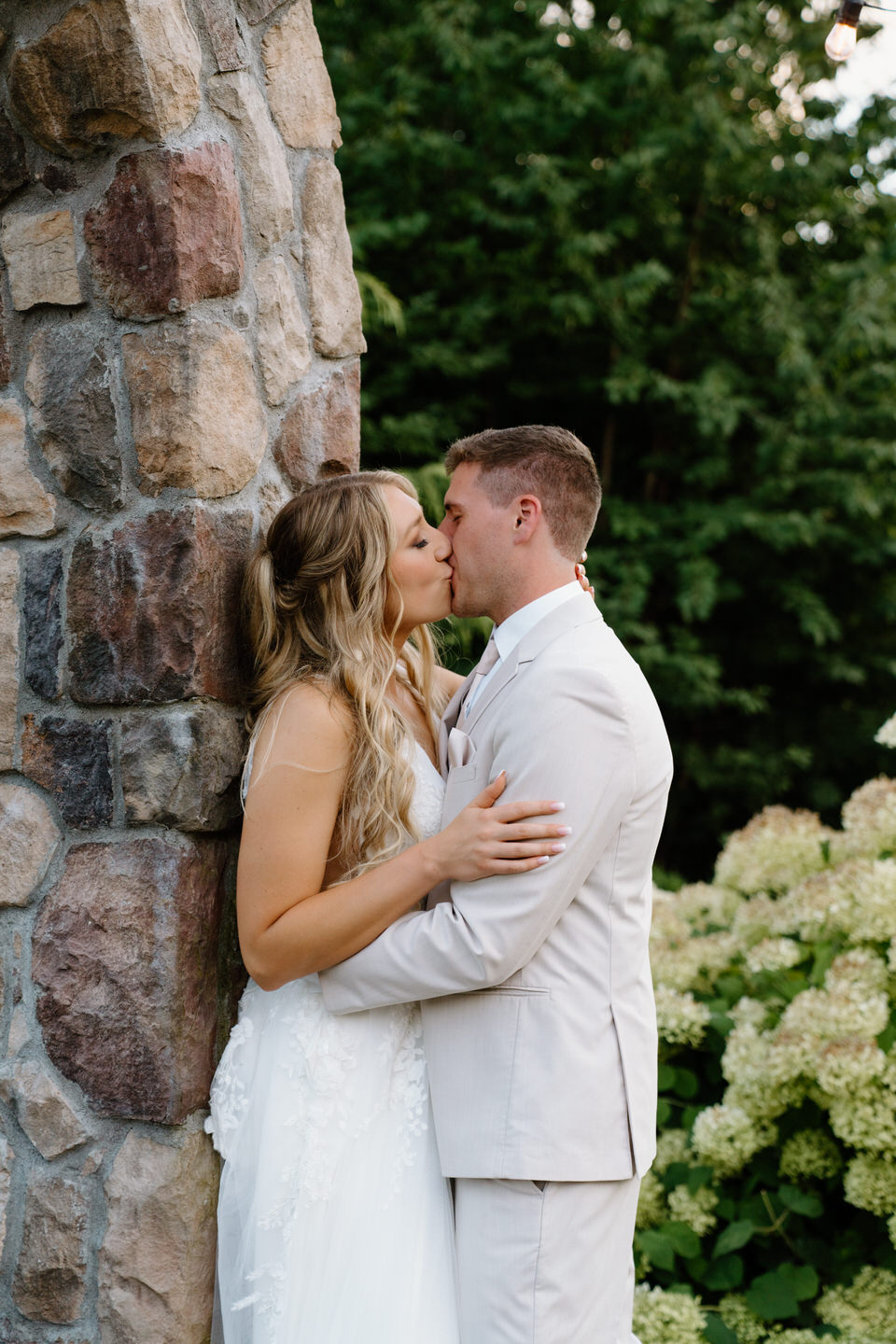 Groom kisses his bride while she is leaned against the stone arch at Cape Horn Estate.