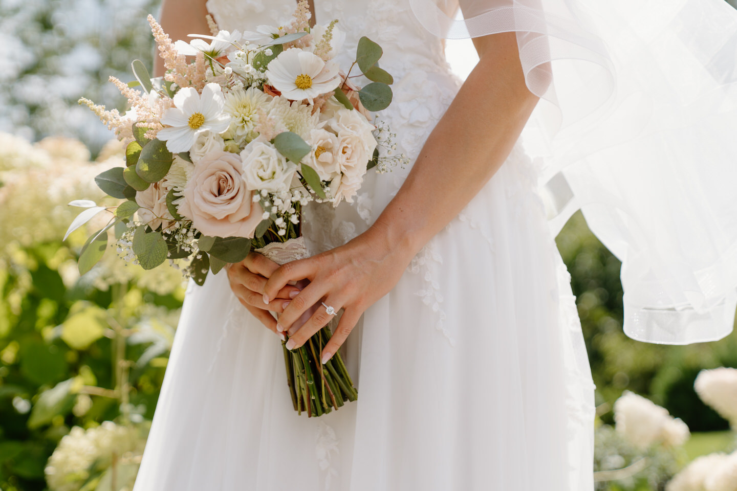 Close up of bride's engagement ring holding her light pink and white bouquet.
