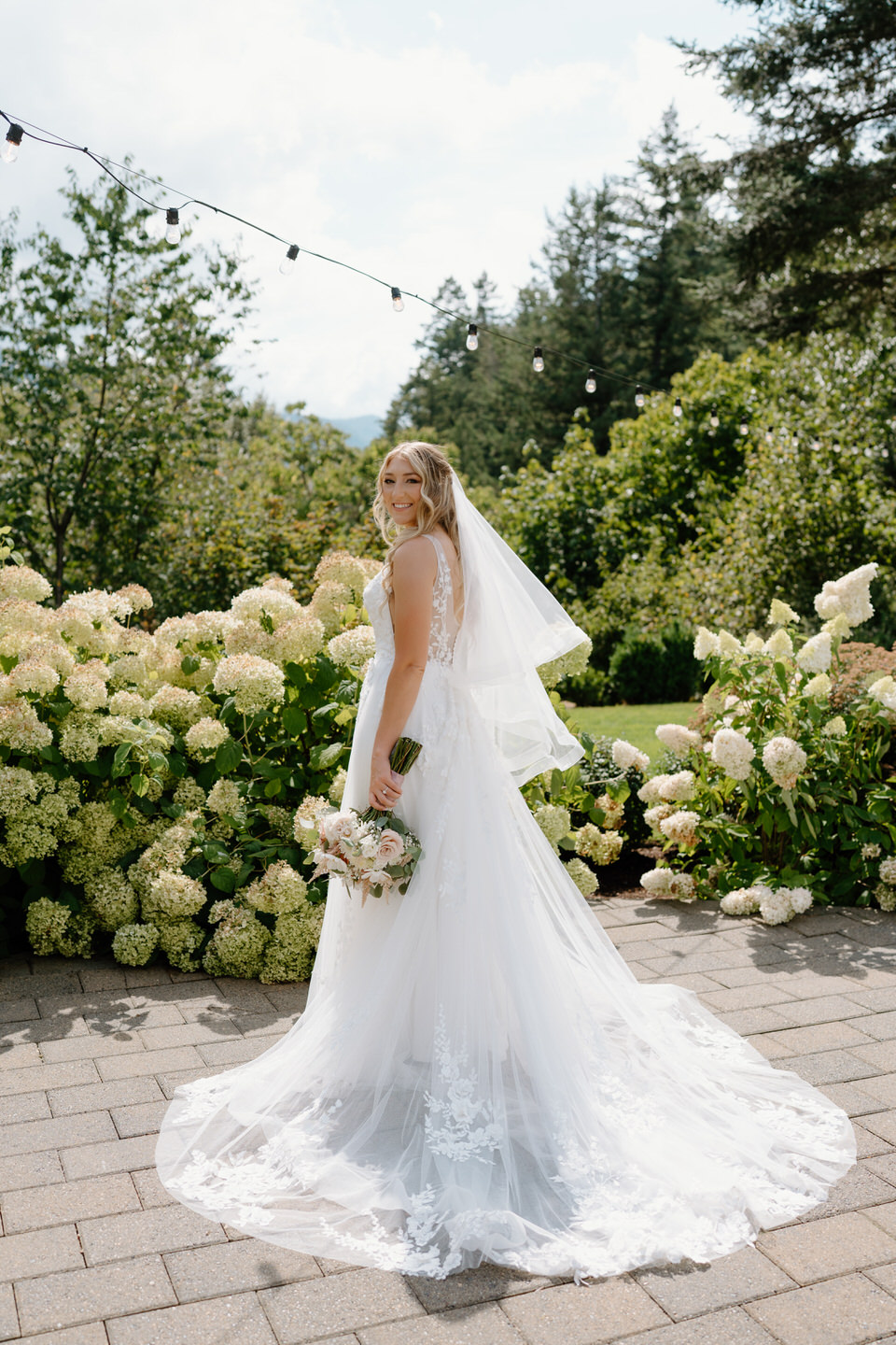 Bride looking over her shoulder at the Cape Horn Estate landscape, surrounded by lush garden flowers.