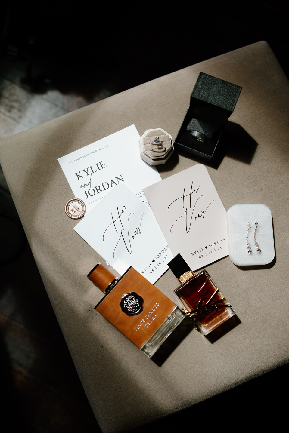 Flat lay details of a wedding, including invitations, vow books, perfume, and rings.