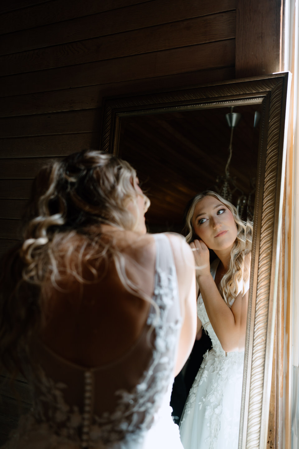 Photo in the mirror of a bride putting in her earrings. 