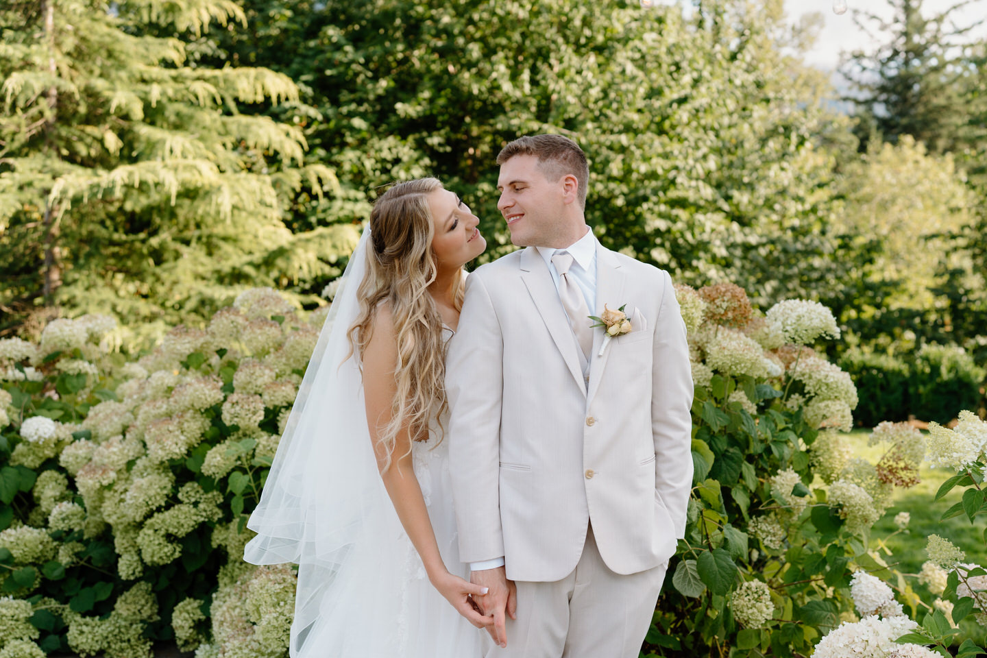 Bride reaches around to hold groom's hand, smiling at each other.