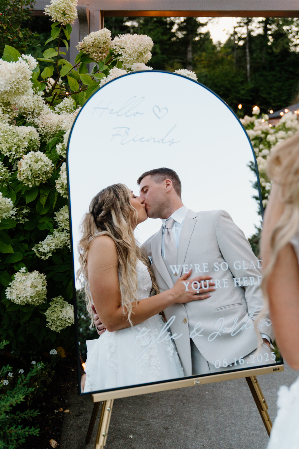 Bride and groom kissing, seen in the mirror that doubles as a wedding welcome sign.