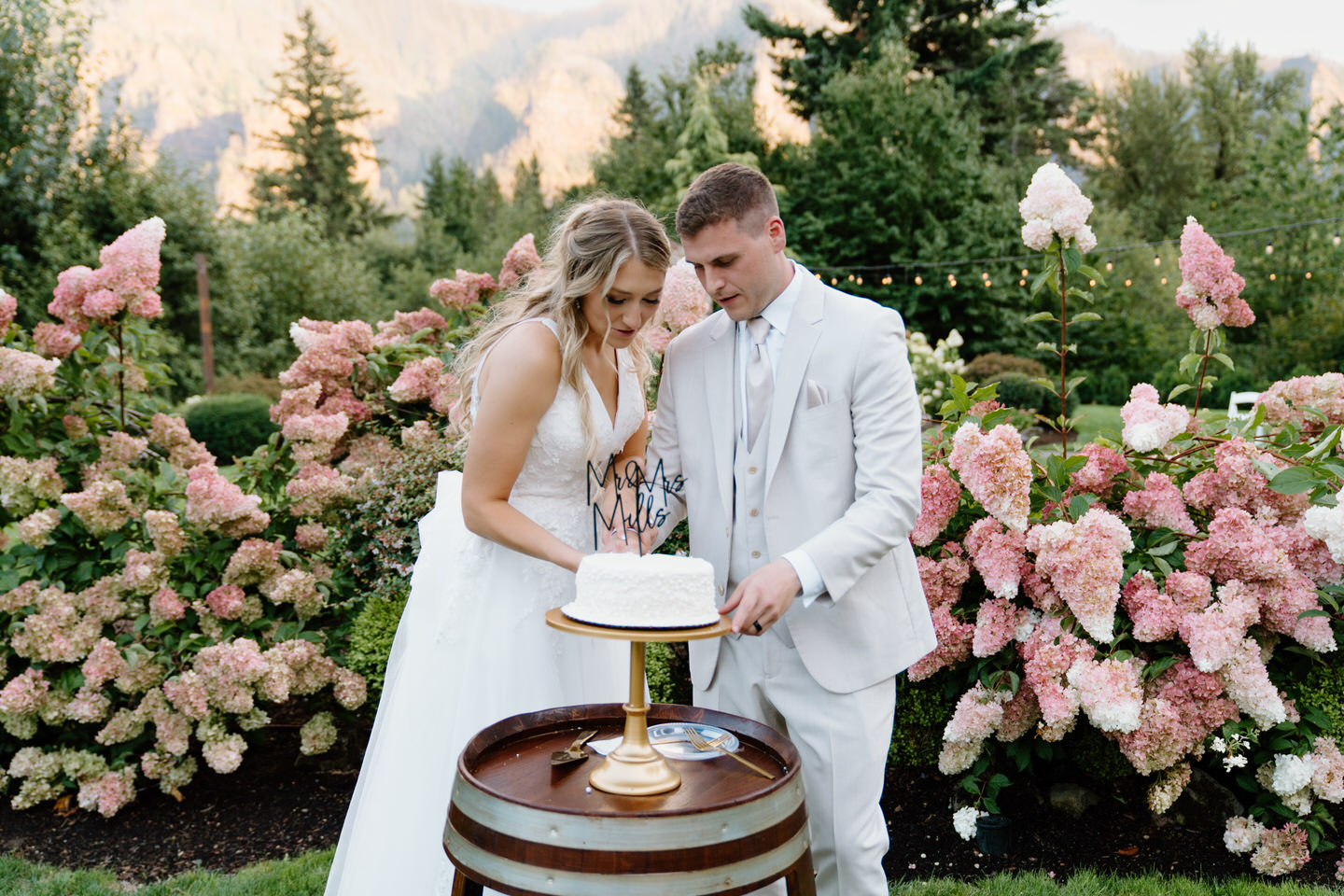 Couple cuts their wedding cake in front of pink flowers.